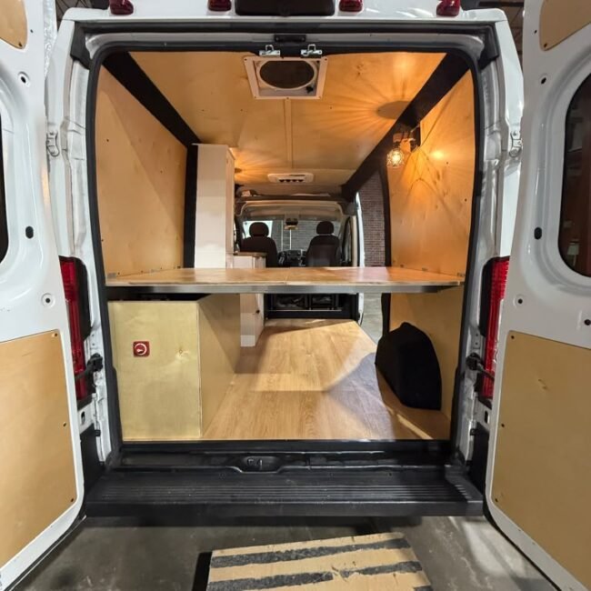 Rear view of the camper van with open doors, raised platform and wood interior.
