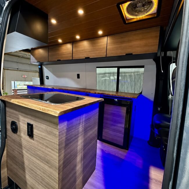 Sprinter camper kitchen with wood surfaces, sink, refrigerator and blue accent lighting.